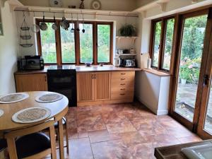 a kitchen with wooden cabinets and a table and some windows at Fig Tree Cottage in Dursley