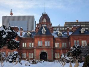 un grand bâtiment en briques rouges avec de la neige au sol dans l'établissement Room 305 Aruter Hotel Sapporo 10-minute walk from Sapporo Station Japanese modern room - Vacation STAY 18410, à Sapporo