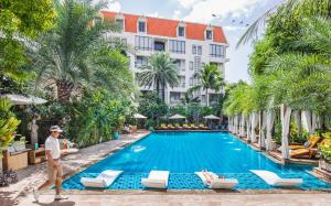 a man walks by a swimming pool in front of a hotel at Palace Gate Hotel & Resort by EHM in Phnom Penh