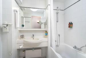 a white bathroom with a sink and a bath tub at elaya hotel noerdlingen, Trademark by Wyndham in Nördlingen