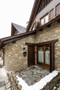 une maison en pierre avec une porte en bois et de la neige dans l'établissement Casa Rústica - Sorieus Lodge en Lérida, à Bossost