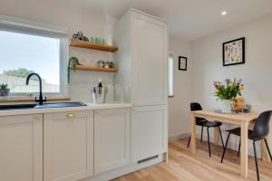 eine Küche mit weißen Schränken und einem Tisch und einem Fenster in der Unterkunft Bryniau Pair Ucha Cottage in Gwytherin + 8 Fotos