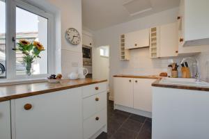 a kitchen with white cabinets and a clock on the wall at Old Mill Cottage in Gweek +8 photos