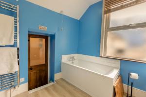 ein blaues Bad mit einer Badewanne und einem Fenster in der Unterkunft Shipwrights Cottage - Appledore in Appledore + 18 Fotos