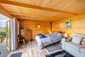 a bedroom in a wooden cabin with a bed and a couch at Latchley Meadows Lodge in Sydenham Damerel