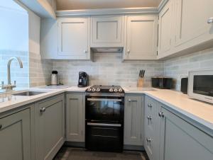 una cucina con armadi bianchi e forno nero di Mill Race Cottage a Chapel Stile