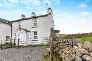 una antigua casa blanca con una pared de piedra en Low Dog Kennel, en Cartmel