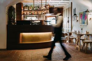 a woman walks past a bar in a restaurant at Strasserwirt - Ansitz zu Tirol in Strassen +100 photos