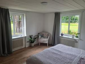 a bedroom with a bed and two windows and a chair at Hus i Småland in Eksjö