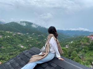 a woman sitting on top of a roof looking at the mountains at Valley View at Twin Oaks in Dharampur