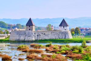 an old castle with two towers on a river at Studio apartman "DJED" in Hrvatska Kostajnica