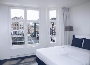 a bedroom with a white bed and two windows at Canal House Inn in Amsterdam