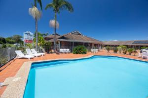 a swimming pool in front of a house with palm trees at Island Palms Motor Inn in Forster