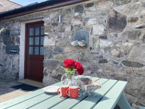 a table with a vase of flowers and two cups at Ysgubor in Y Felinheli