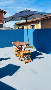 Una mesa de picnic con una sombrilla junto a una pared azul. en Pousada Mar e Sol, en Peruíbe