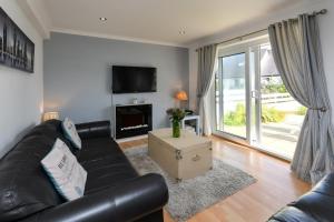 a living room with a black leather couch and a tv at 243 Cae Du in Abersoch