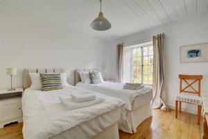 two beds in a white room with a window at The White Cottage in Saint Winnow