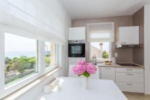 a white kitchen with a vase with pink flowers on a table at Apartment & Room Ladisic in Orasac