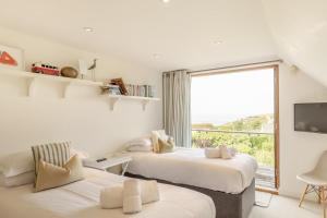 two beds in a room with a large window at Higher Close in Mawgan Porth