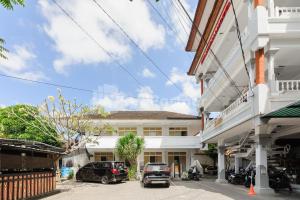 a white building with cars parked in a parking lot at Pulau Bali Hotel Denpasar RedPartner in Denpasar