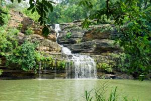 a waterfall in the jungle next to a pond at Vindhyavan Mud House in Panna