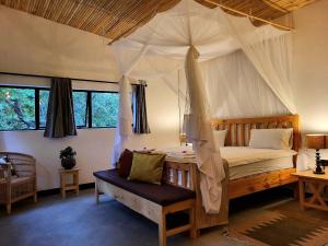 Un dormitorio con una cama con dosel y un banco en ella. en Ntchisi Forest Lodge, 