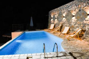 a swimming pool with chairs and a stone wall at Luxury Villa Marija Panoramic Pool & Nature Retreat in Podgorica