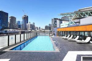a swimming pool on the roof of a building with chairs at Lovely 2 Bedroom Apt at Marvel Stadium with Car Park and Rooftop Pool in Melbourne