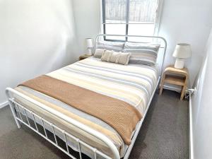 a white bed with a striped blanket and a window at Kahibah Guesthouse in Kahibah