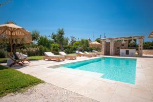 a swimming pool with lounge chairs and an umbrella at I Trulli del Tarassaco with private pool by Pregio Villas in Martina Franca
