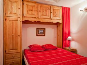 a bedroom with a bed with red sheets and wooden cabinets at Appartement Centre-Ville avec Terrasse à Brides-les-Bains, Proche Télécabine et Spa - FR-1-512-138 in Brides-les-Bains