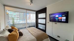 Un dormitorio con una cama con un televisor de pantalla plana en la pared. en Mall Parq Arauco Tranquilo y Familiar Las Condes, en Santiago