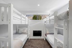 two white bunk beds in a room with a tv at Getaway on Galloway - Close to the Lake in Wanaka