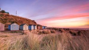 a row of beach huts on the beach at sunset at Coastal home sleeping five - 2 minute walk beach in Pakefield