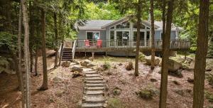 a house with a deck and stairs in the woods at Sunset Heaven 3 Bedroom Lakefront Retreat in Bracebridge