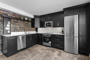 a kitchen with black cabinets and a stainless steel refrigerator at Hotel Manoir D'Auteuil - Par Aneyro in Quebec City