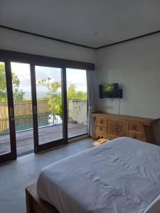 Un dormitorio con una cama y un televisor y un balcón. en Green Bowl Beach Villas, en Uluwatu 29 fotos más