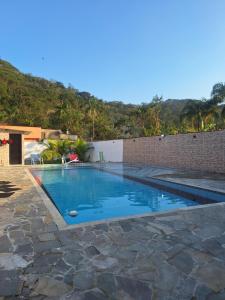 a swimming pool with a brick wall and blue water at Casa em Bertioga com piscina aquecida Sitio família ROCHA in Bertioga