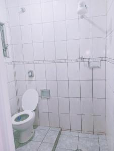 a white tiled bathroom with a toilet and a shower at kit net Vovó nice garagem gratis in Aparecida