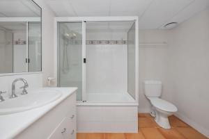 a white bathroom with a shower and a toilet at Steps from The Strand 2BR & 2BA Riveria Retreat Pool & Castle Hill Views in North Ward