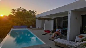 a woman sitting on a chair next to a swimming pool at NEW- Ericeira Design Villa- 10 min from Beach, pool and great view in Ericeira