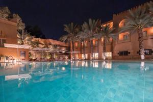 a large swimming pool with palm trees in front of a hotel at Amanar Hôtel & Spa Ouarzazate in Ouarzazate