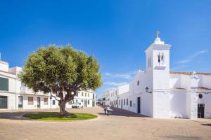 a tree in the middle of a street next to a church at Tramontana 113 P1 by 3VILLAS in Fornells