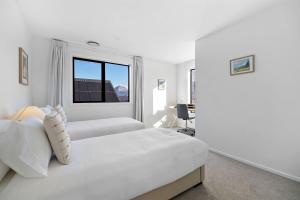 a white bedroom with two beds and a window at Alpenglow Lodge with steam sauna in Queenstown