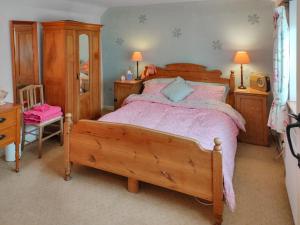 a bedroom with a large wooden bed with pink sheets at Cow Cottage in Langford
