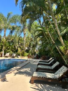 a resort pool with lounge chairs and palm trees at Arco Íris Pousada in Ilha Comprida