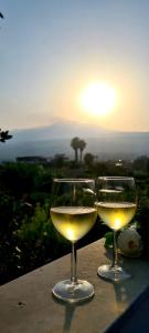 two glasses of white wine sitting on a ledge with the sunset at La mansardina sul mare - Mascali in Mascali
