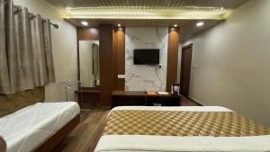 a bedroom with two beds and a tv on the wall at Hotel Shreeji Residency in Pachmarhī