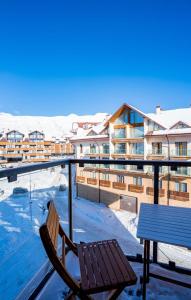a wooden chair sitting on a balcony with snow covered buildings at Evdo Apartments F1 Modern house in Kʼumlistsʼikhe