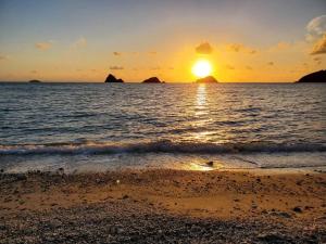 a sunset over the ocean with rocks in the water at 西古見の宿だるま in Setouchi